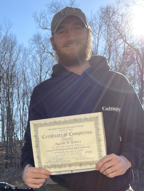 Man outdoors holding certificate near trucks